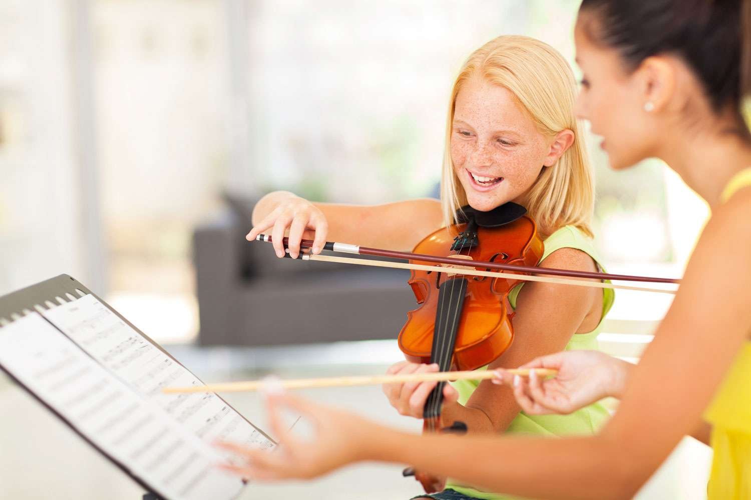happy violin student playing her violin next to her instructor