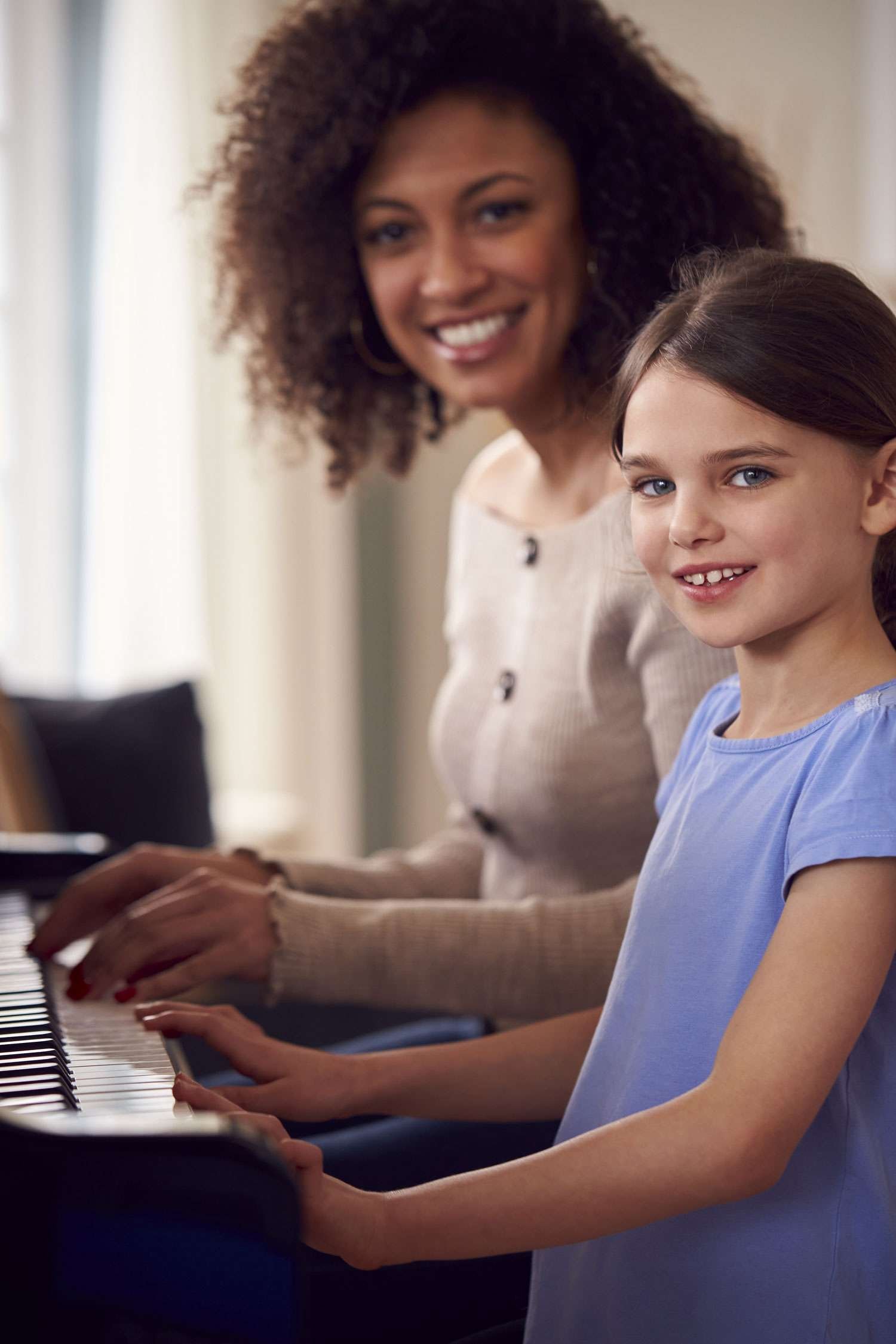 piano instructor and her young female student hands on the piano smiling at the camera