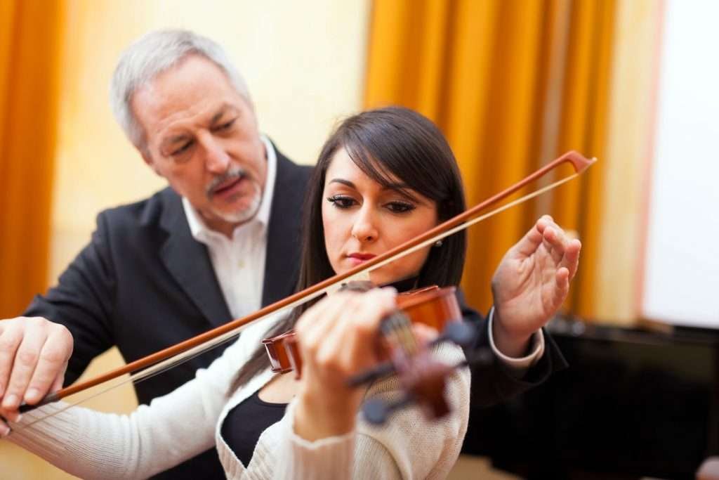 violin instructor assisting his student in playing the violin